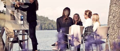 A group of people seated on a wooden deck by a lake, with a person standing and interacting with a poster board.