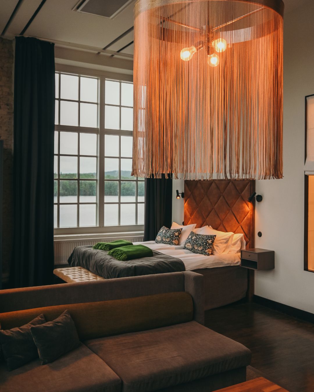 Un dormitorio moderno con cama, sofá, lámpara colgante y vistas al exterior.