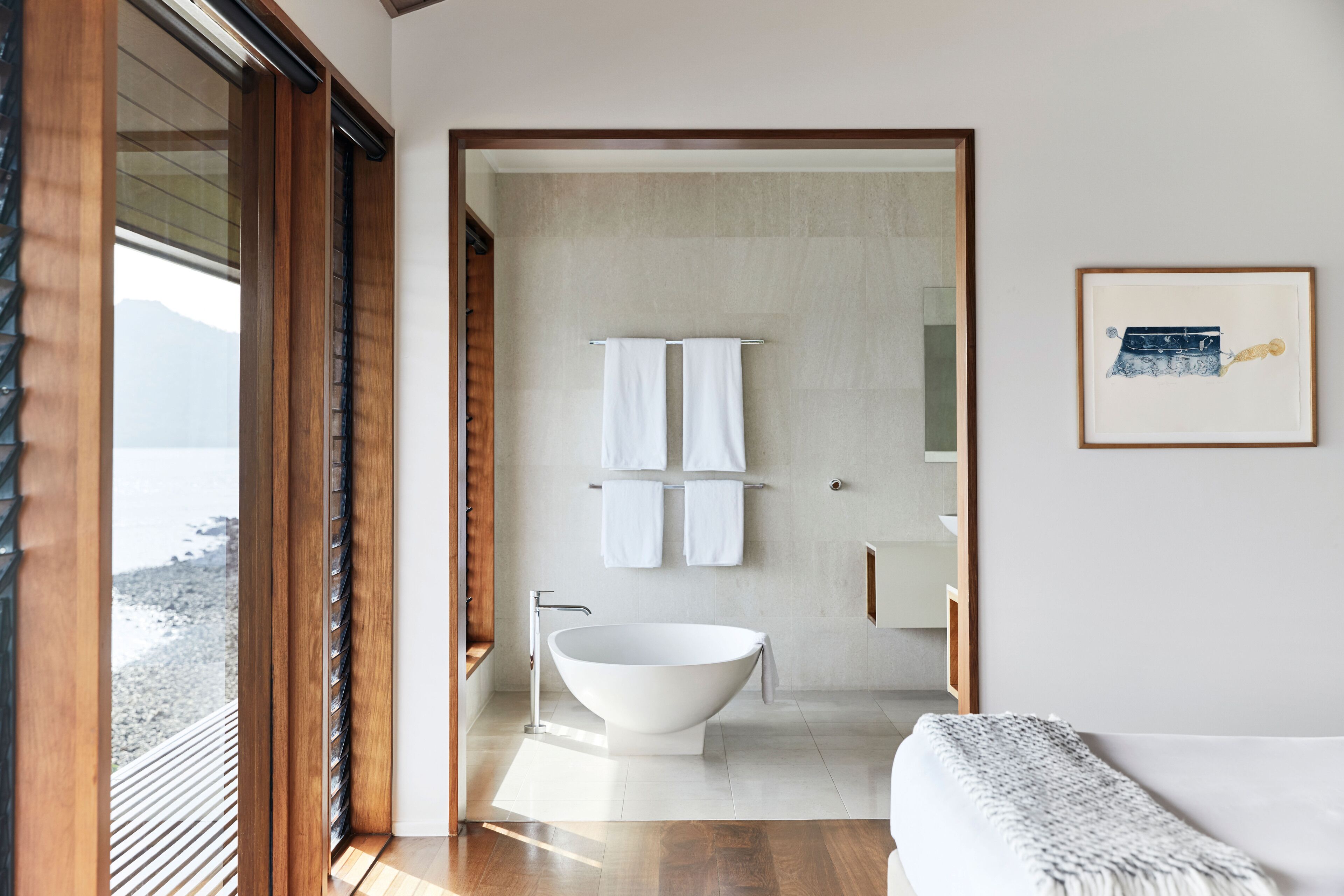 A modern bathroom with a freestanding bathtub, a towel rack with two towels, and a framed picture on the wall.