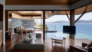 A modern living room with a stone wall, wooden furniture, a pool, and a TV. - Qualia (Whitsundays)