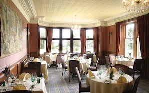 Comedor con varias mesas dispuestas para el servicio, ventanas amplias con cortinas y un candelabro.