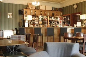 Una zona de bar con mostrador de madera, varias sillas y una mesa de comedor con mantel escocés.