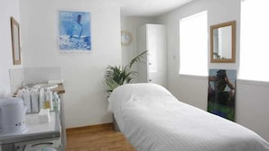 A bedroom with a bed, a bedside table, a mirror, a poster on the wall, and a window.