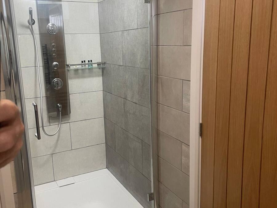 A shower area with a glass door, tiled walls, and a wooden door adjacent to it.