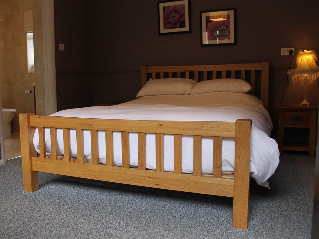 A wooden bed with a headboard, a bedside table with a lamp, and two framed pictures on the wall.