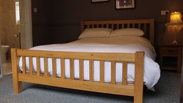 A wooden bed with a headboard, a bedside table with a lamp, and two framed pictures on the wall.