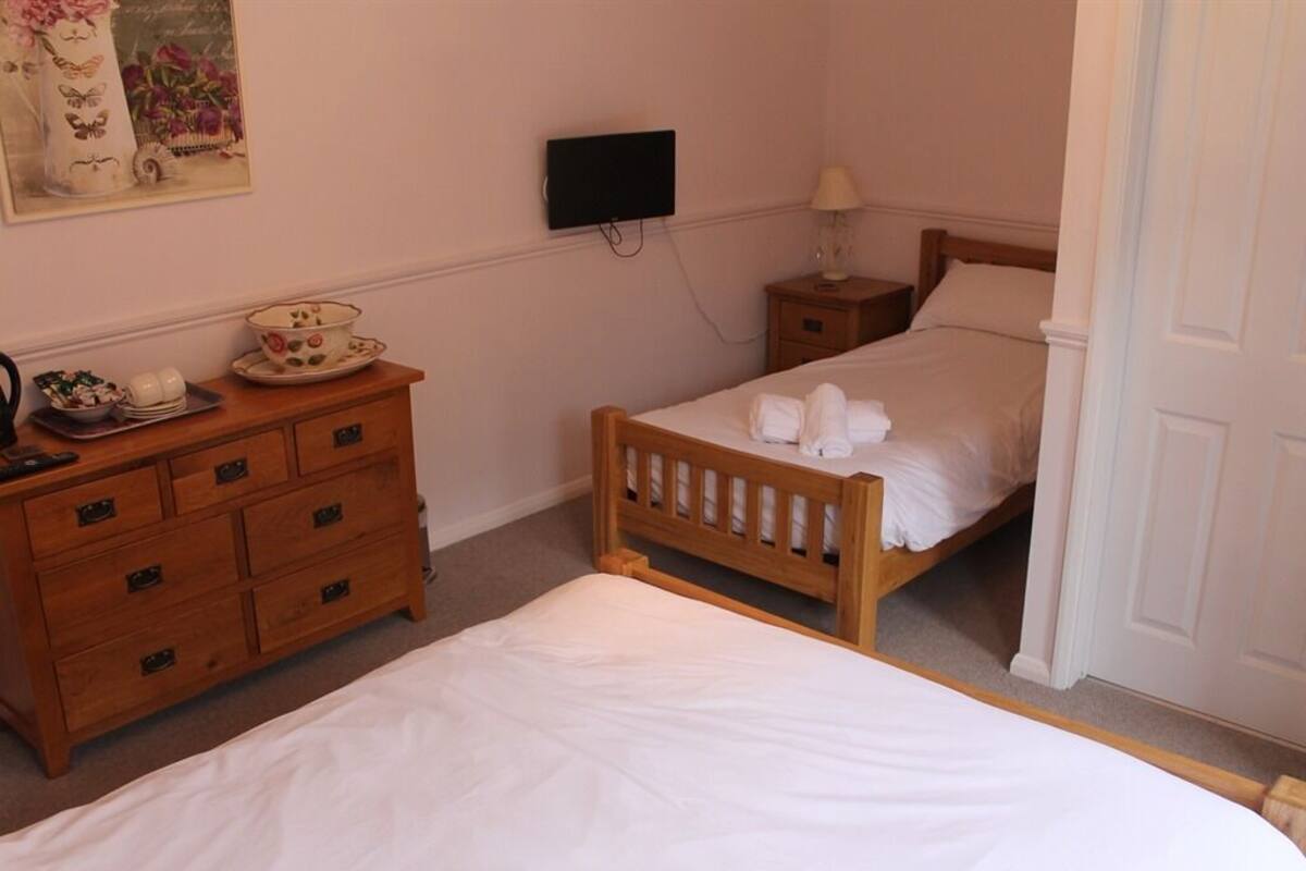 A bedroom with a wooden bed, a bedside table with a lamp, a dresser, and a television mounted on the wall.