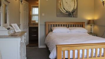 A bedroom with a wooden bed, a desk with a telephone, a mirror, and a painting on the wall.