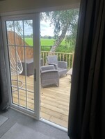 Une porte-fenêtre coulissante donne sur une terrasse extérieure aménagée avec des meubles en osier et offre une vue sur un champ verdoyant.