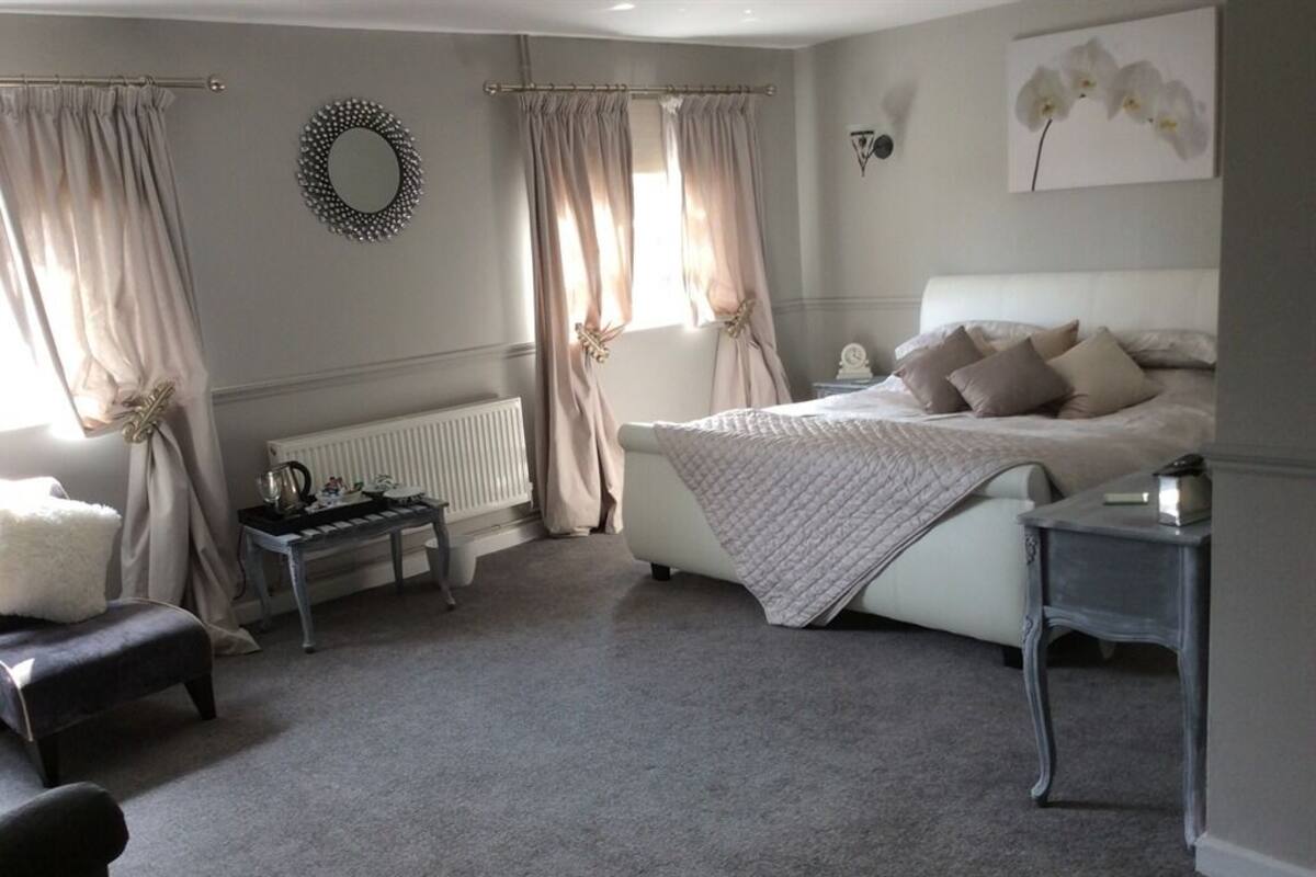A bedroom with a bed, a bedside table, a radiator, and curtains.
