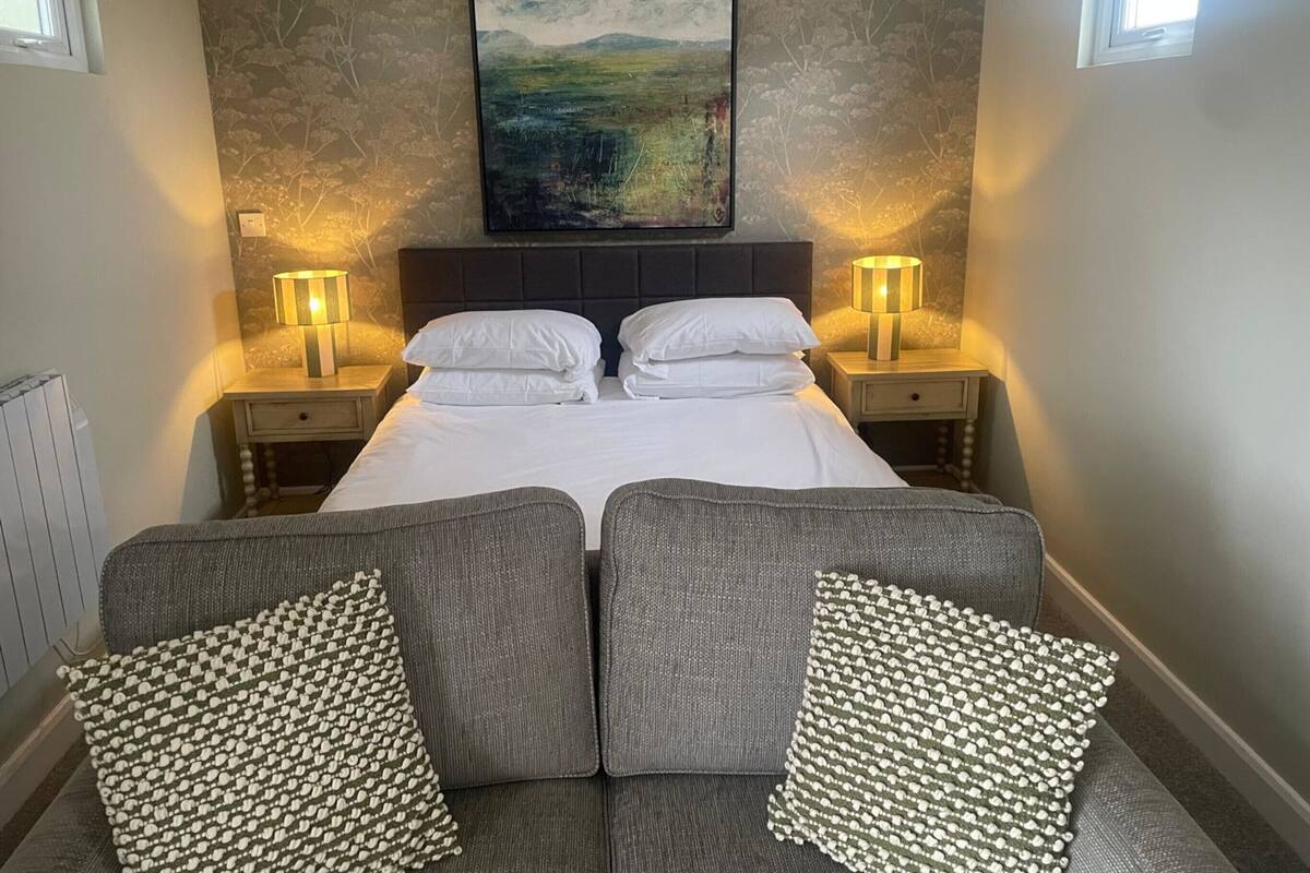 A neatly arranged bedroom with a bed, two bedside tables, two lamps, and a large painting on the wall.