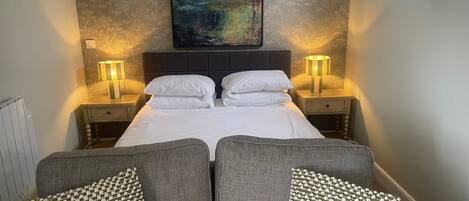 A neatly arranged bedroom with a bed, two bedside tables, two lamps, and a large painting on the wall.