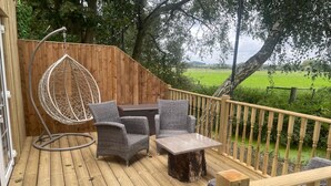 A wooden deck with wicker furniture, including a chair and a table, and a hanging chair. - The Swan Motel (Beccles)