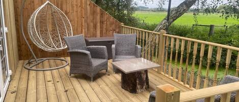 A wooden deck with wicker furniture, including a chair and a table, and a hanging chair.