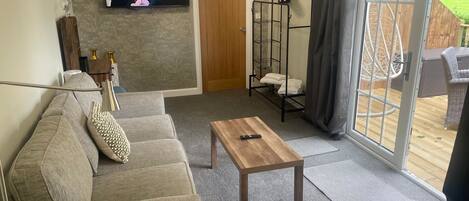 A living room with a sofa, a coffee table, a TV, a door, a metal rack, and a view of the outdoors.
