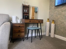 Habitación de hotel compacta con un escritorio de madera, una pequeña silla azul, una cafetera blanca y dos jarrones decorativos.