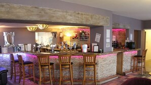 A bar area with wooden chairs, a bar counter, and a seating area with tables. - The Swan Motel (Beccles)