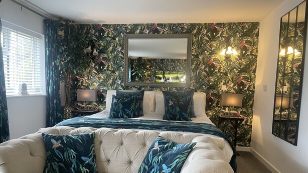 A bedroom with a large bed, two nightstands, a mirror, and a decorative wall. - The Swan Motel (Beccles)