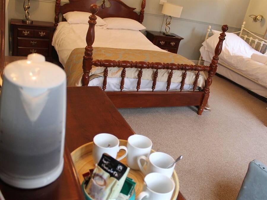 A hotel room with a wooden four-poster bed, a bedside table with a lamp, and a tray with cups and a teapot.