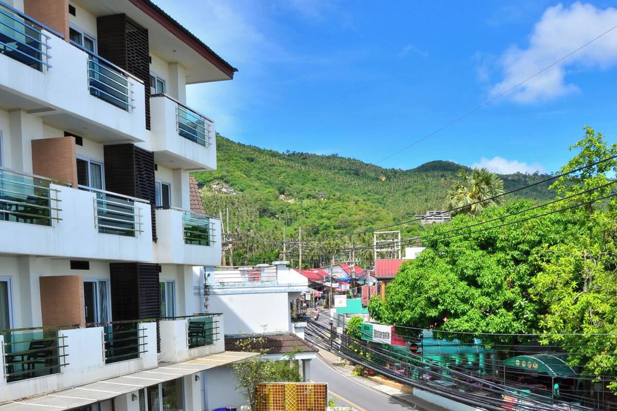 A hotel with a swimming pool, multiple balconies, and a view of a green hillside.