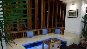 Un vestíbulo moderno con zona de estar, una mesa de centro de vidrio y un banco de madera con cojines azules.