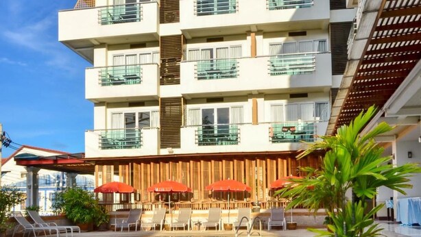 Un hotel con piscina, mobiliario exterior y varios balcones.