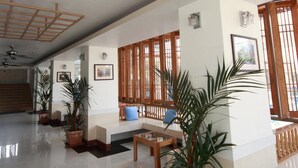 Un vestíbulo amplio con ventilador de techo, plantas en macetas, muebles de madera y ventanas grandes.