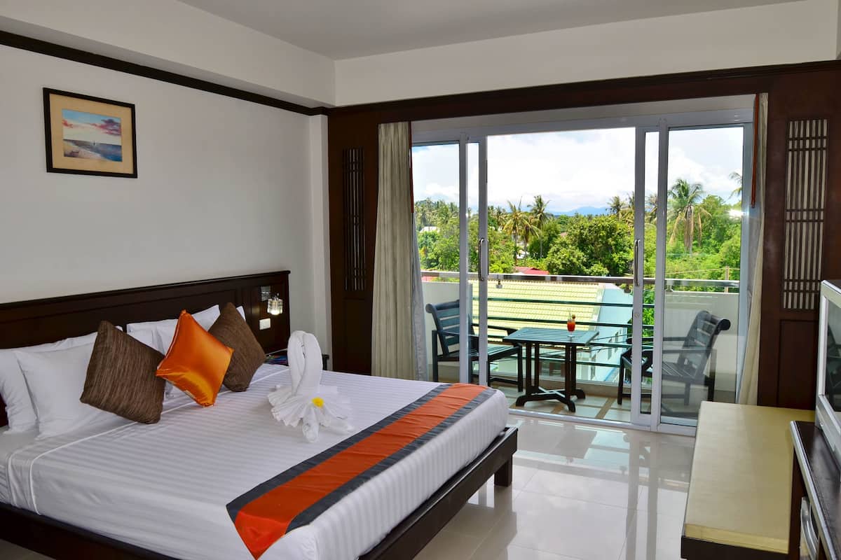 A hotel room with a large bed, a TV, and a balcony with a table and chairs.