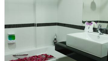 Un baño con una bañera llena de pétalos de rosa, un lavamanos blanco y un espejo sobre él.