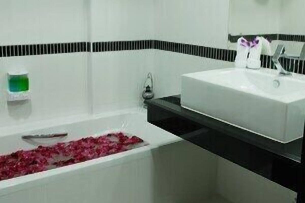 A bathroom with a white sink, a mirror, and a bathtub with rose petals.