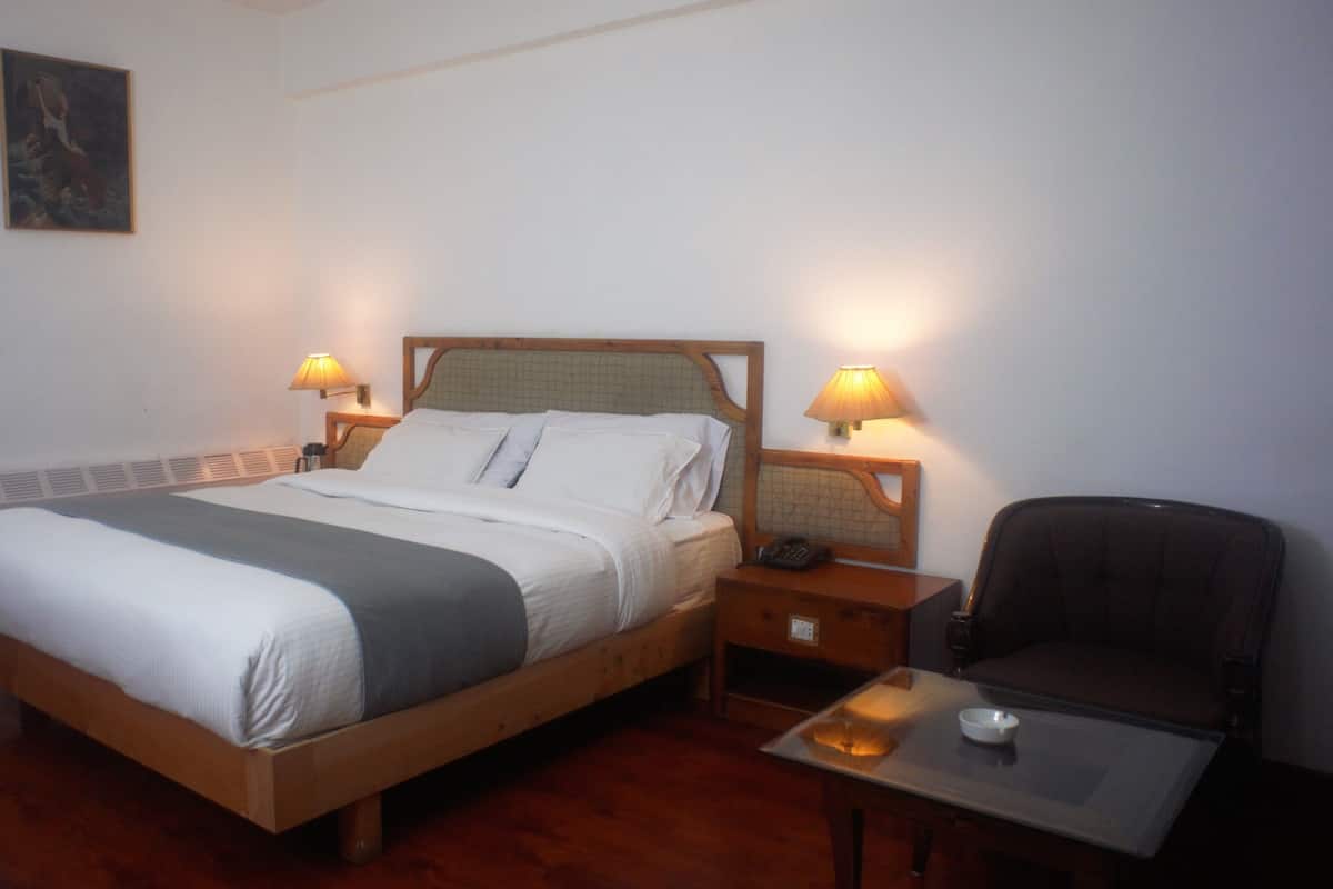 A hotel room with a wooden bed, two bedside lamps, a chair, and a small table.