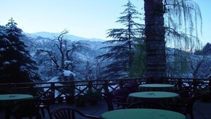 A patio with round tables and chairs, overlooking a snowy mountainous landscape. - Banon Resorts (Manali)