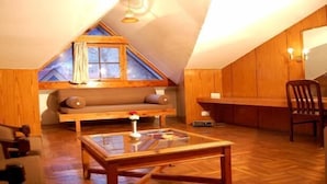 A cozy loft bedroom with a sloped ceiling, a wooden bench, a glass coffee table, and a wooden chair. - Banon Resorts (Manali)
