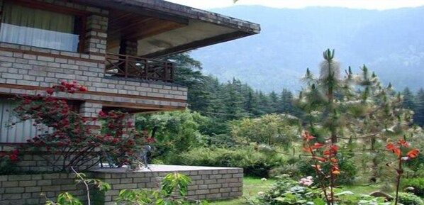 A two-story building with a balcony, surrounded by a garden with various plants and flowers. - Banon Resorts (Manali)