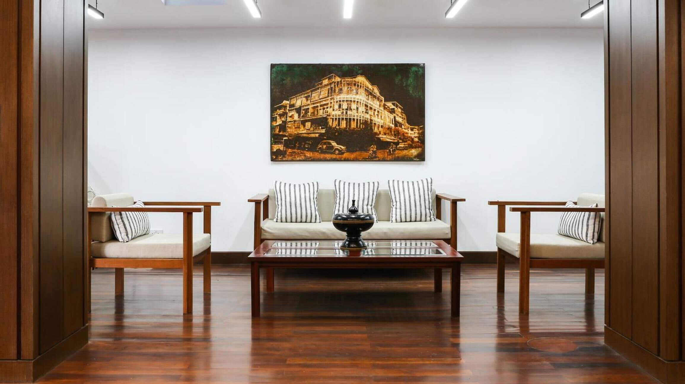 Une pièce dotée d’un plancher en bois, de deux canapés avec des coussins à rayures, d’une table basse au centre et d’un grand tableau encadré accroché au mur.