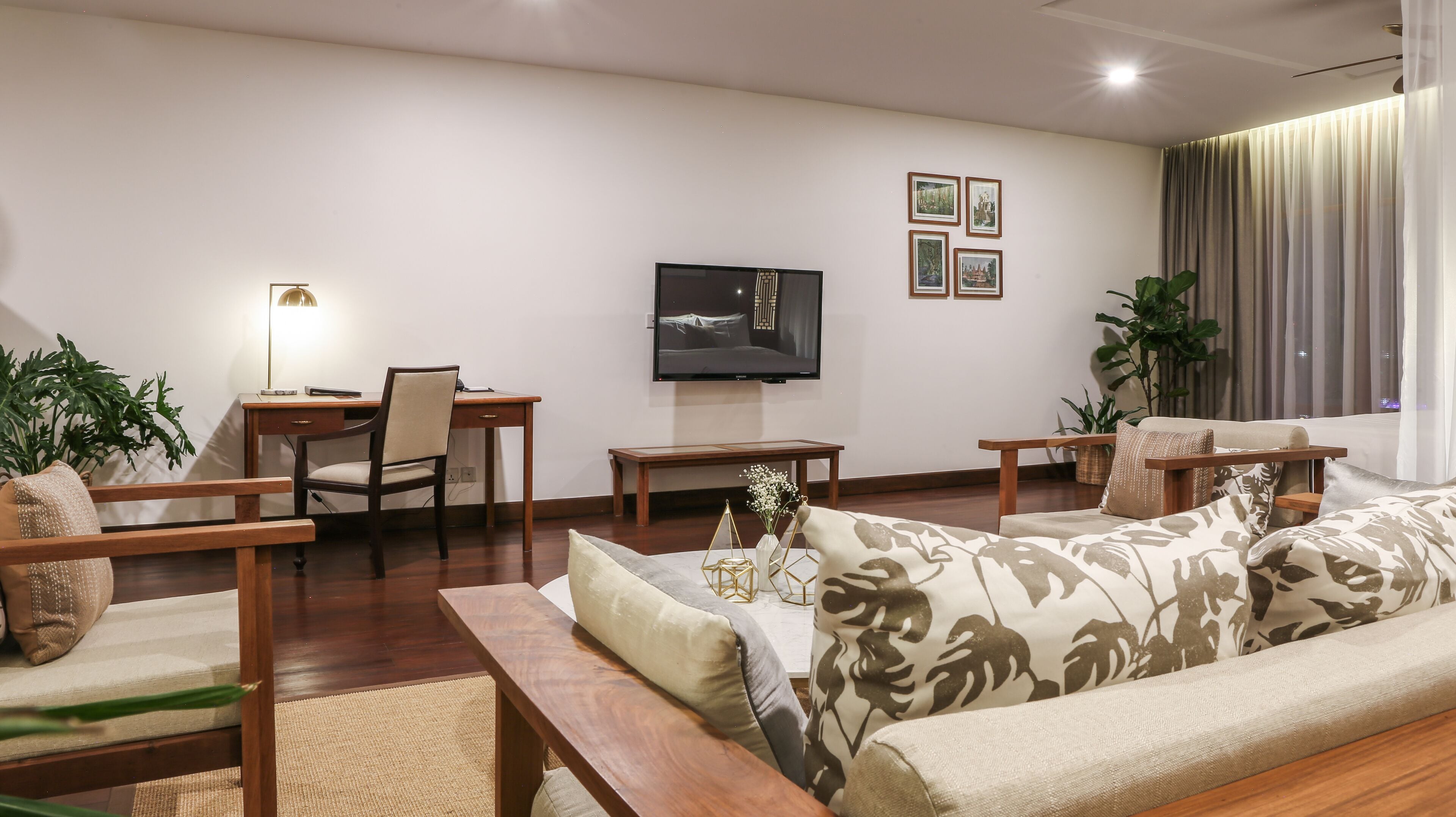Una sala de estar moderna con un sofá, sillones, una mesa de centro, un televisor y cuadros enmarcados en la pared.