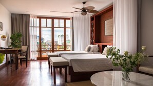 Ein Hotelzimmer mit zwei Betten, einem Esstisch, einem Stuhl, einem runden Couchtisch und Blick auf die Stadt durch große Fenster.
