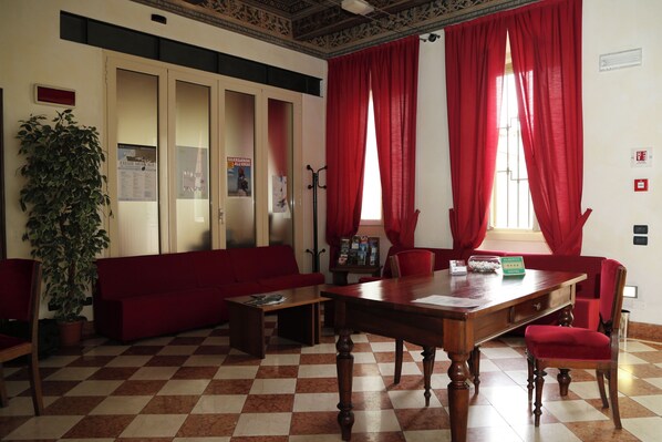 Un hall de hotel con piso a cuadros, muebles rojos, una mesa de madera y una planta en maceta.