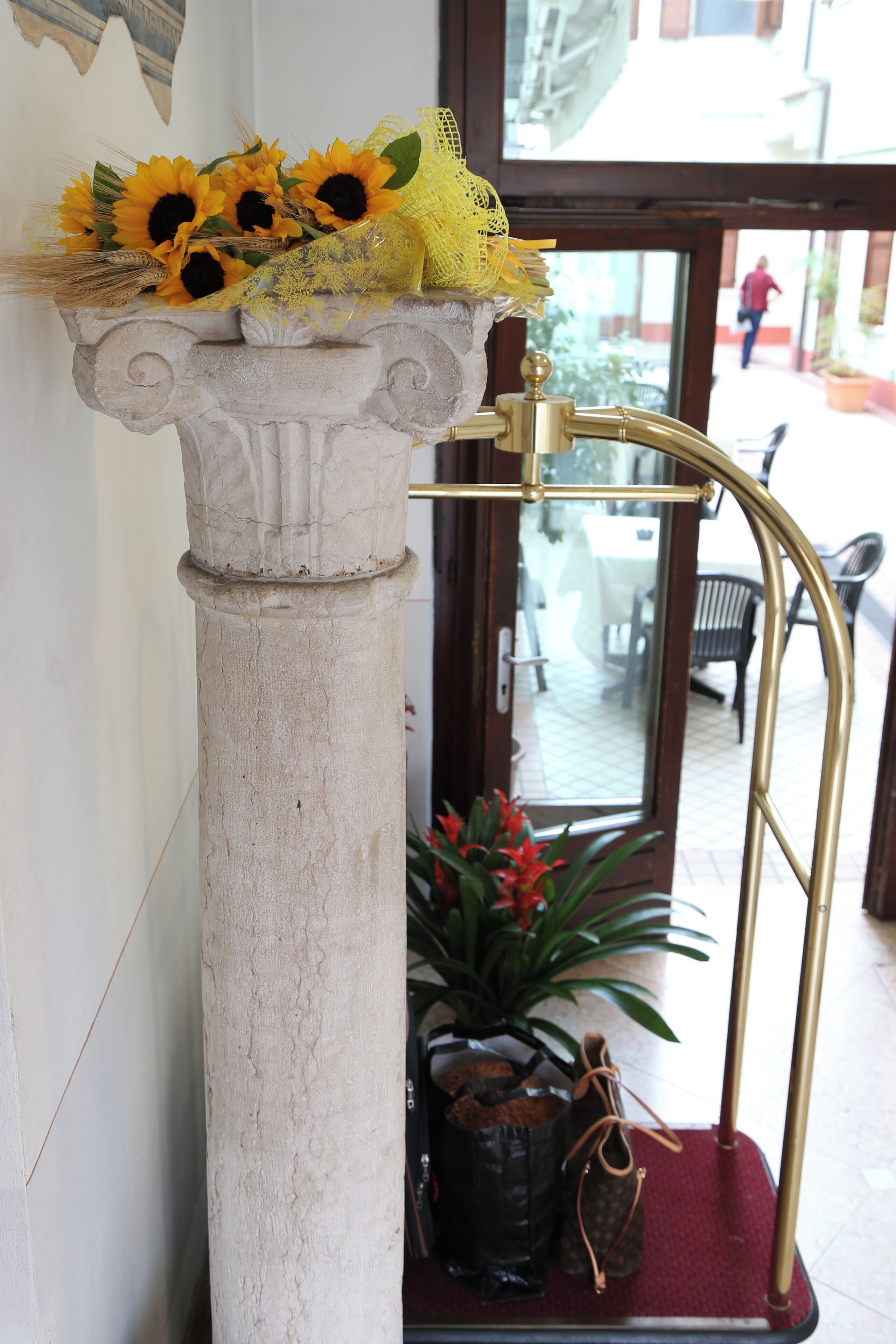 A column with a decorative top, a brass faucet, and a potted plant with red flowers.