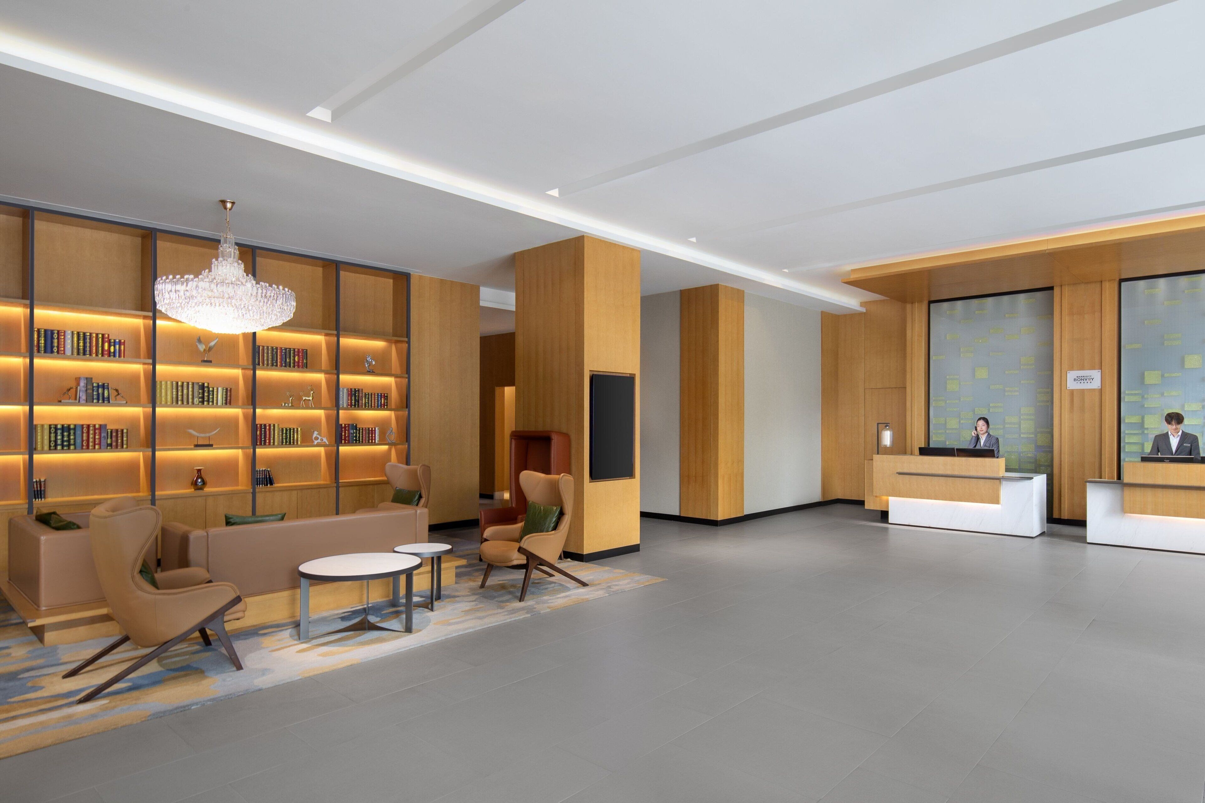 A modern lobby with a reception desk, seating area, and a large bookshelf.