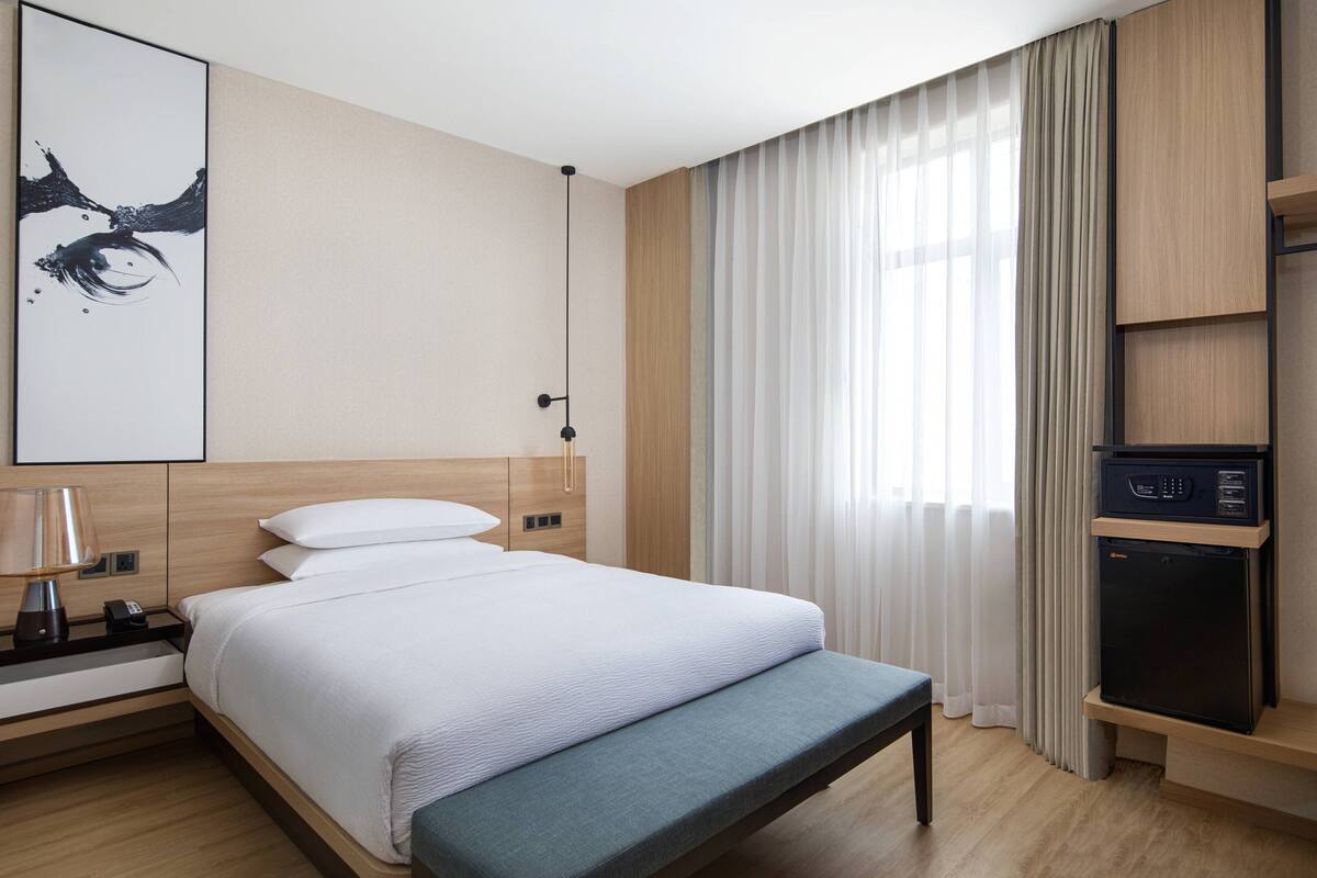 Une chambre d’hôtel moderne équipée d’un lit, d’une table de chevet, d’une lampe et d’un mini-réfrigérateur intégré.