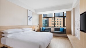 Una habitación de hotel moderna con una cama grande, un área de descanso con vista a la ciudad y un televisor de pantalla plana en la pared.