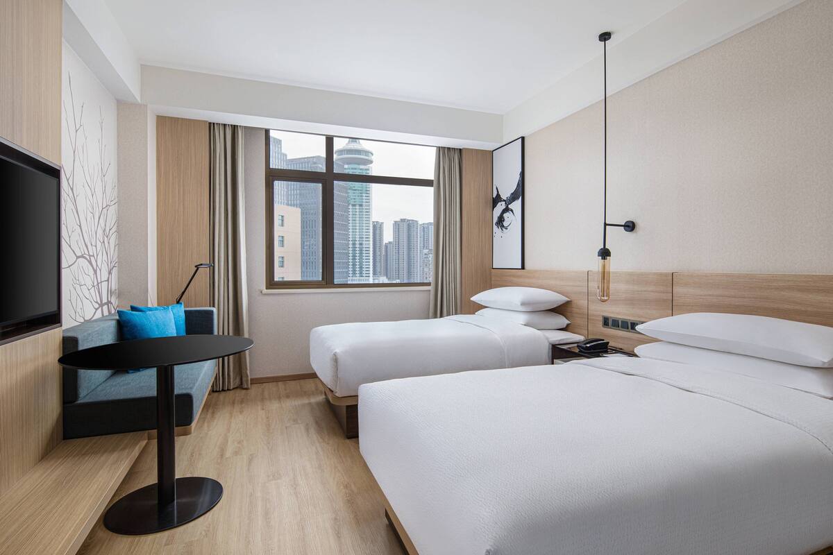 Une chambre d’hôtel avec deux lits, un bureau, une télévision et une grande fenêtre donnant sur la ville.