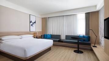 A modern hotel room with a large bed, a sofa, a small table, and a TV.