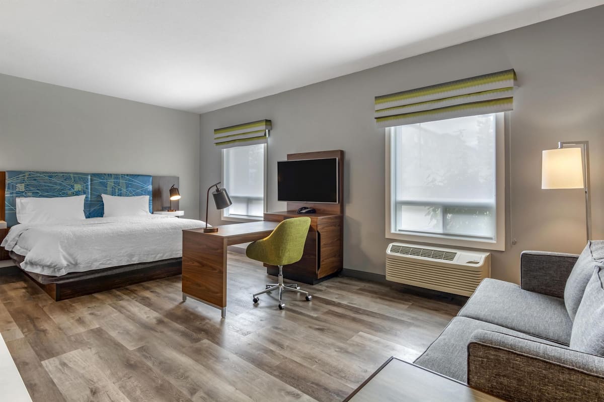 A hotel room with a bed, desk, chair, TV, and a sofa.