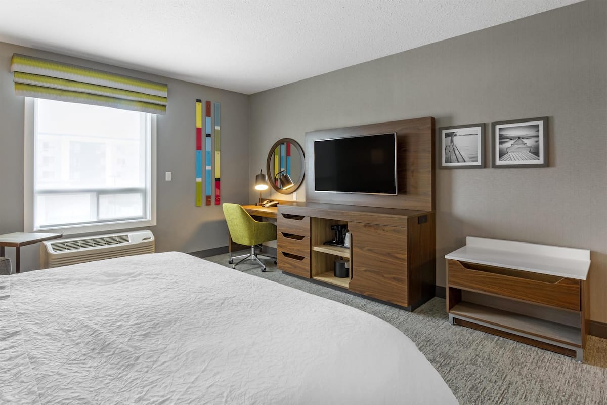 A modern hotel room with a large bed, a desk with a chair, a flat-screen TV, and a small seating area.