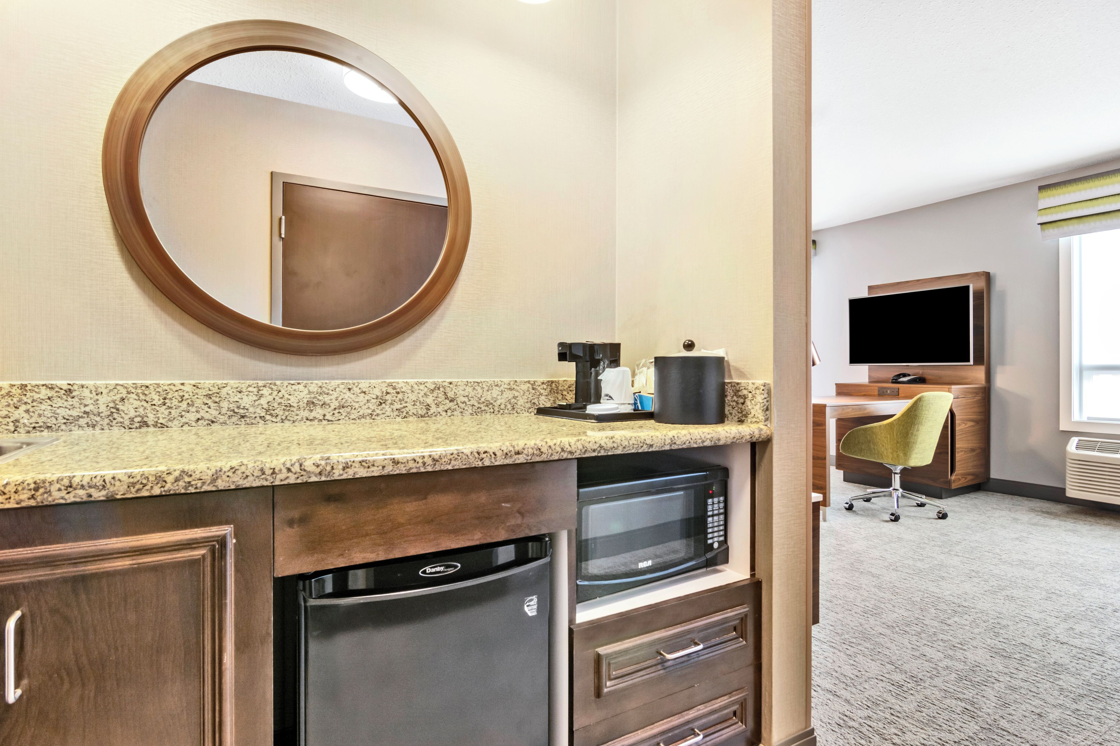 Habitación de hotel con zona de cocina equipada con microondas, lavavajillas y cafetera.