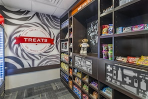 Un espace dédié aux en-cas, avec un panneau indiquant « Friandises », une variété de collations et de boissons, et un ours en peluche placé sur une étagère.
