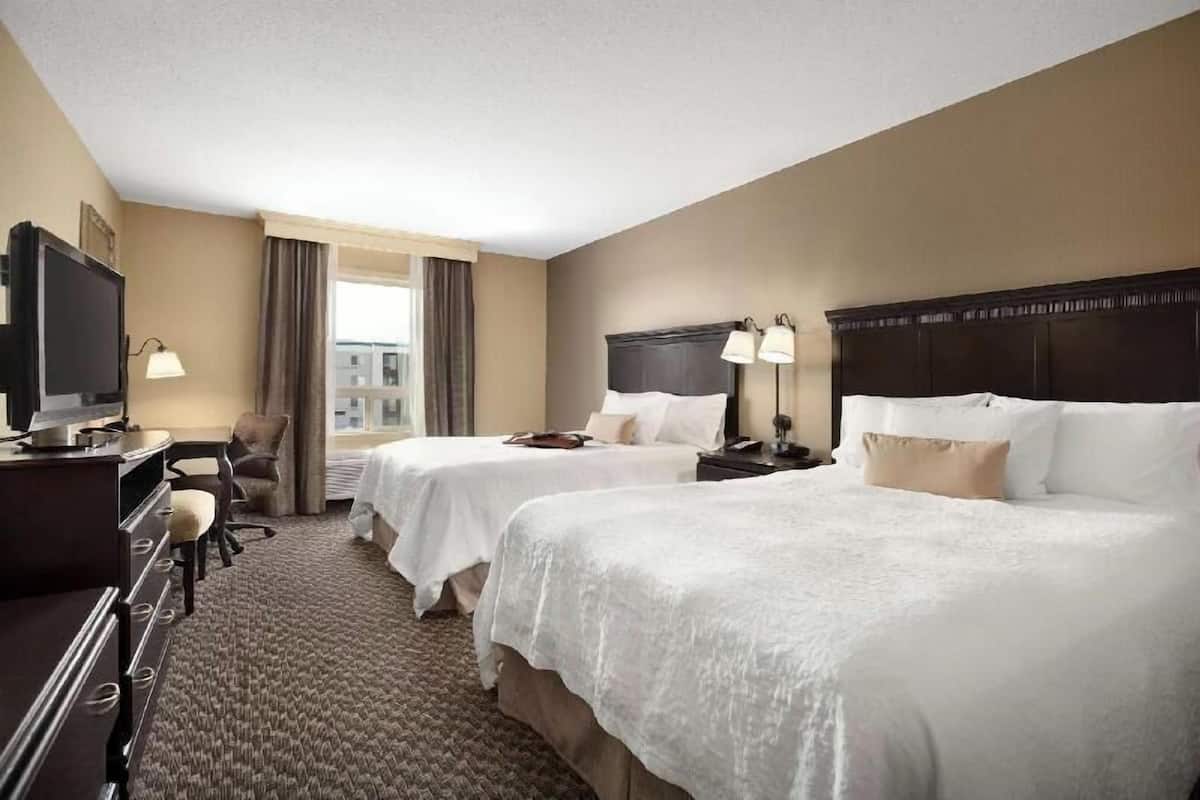 A hotel room with two beds, a desk with a television, a chair, and a window with curtains.