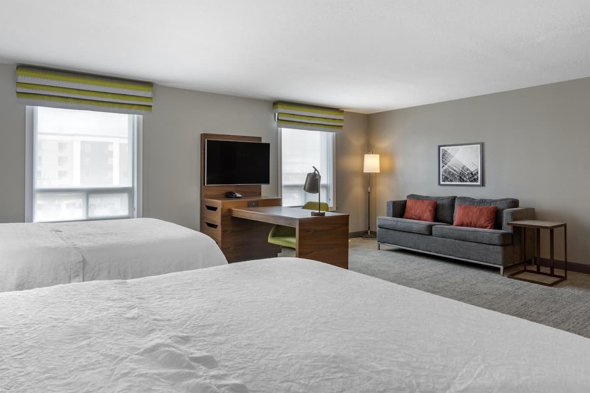 A hotel room with two beds, a desk with a flat-screen TV, a sofa, and a lamp.